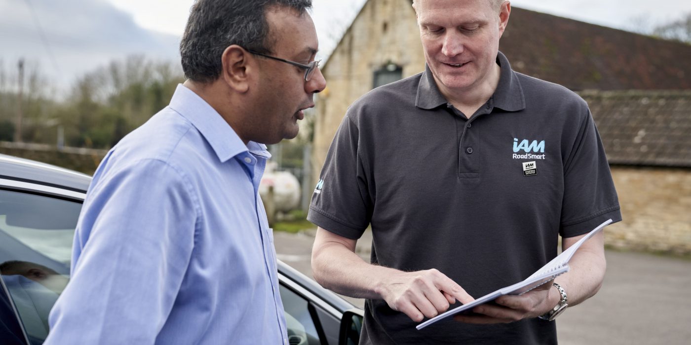 An IAM RoadSmart instructor reviews the drivers manual with a student outside the car